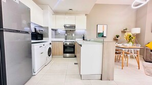 Una cocina moderna con horno empotrado, microondas y lavadora, zona de comedor con mesa y sillas, y una pequeña isla con pileta.