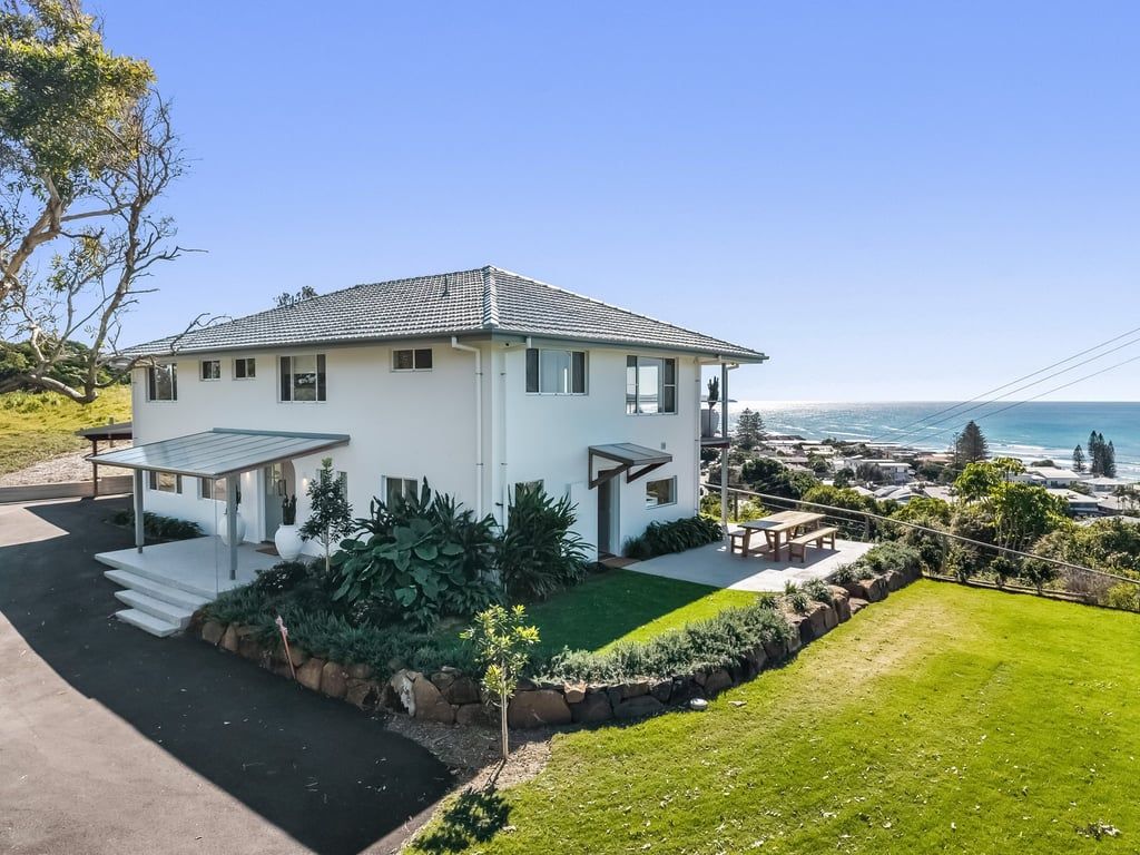 Uma casa moderna de dois andares com telhado plano, varanda coberta e vista para o oceano.