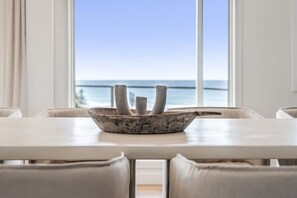 A dining area with a table and chairs, a decorative bowl on the table, and a view of the ocean through large windows. - Whale Watcher - elevated coastal escape (Lennox Head)