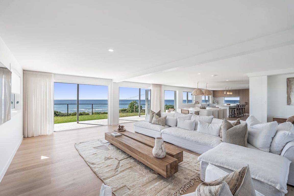 A spacious living room with a large sofa set, a wooden coffee table, and a view of the ocean.