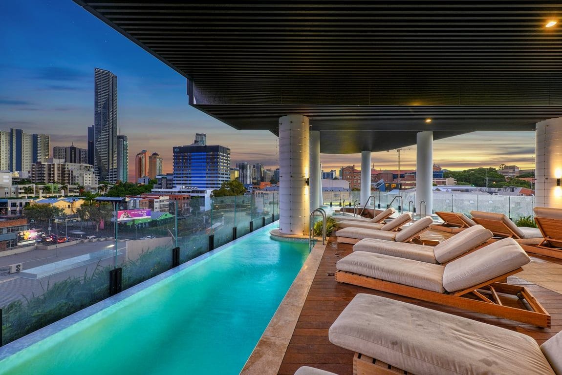 Una piscina sul tetto con poltrone relax, vista sullo skyline cittadino e un design architettonico moderno.