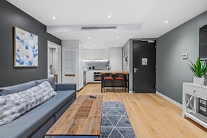 A modern living room with a grey sofa, a wooden coffee table, and a kitchen in the background. - High-Floor Valley Escape | Pool, Gym & Views (Brisbane)