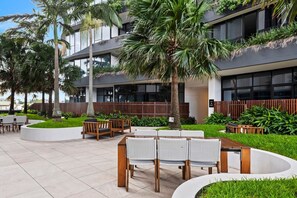 An outdoor seating area with tables and chairs, surrounded by greenery and palm trees. - High-Floor Valley Escape | Pool, Gym & Views (Brisbane)