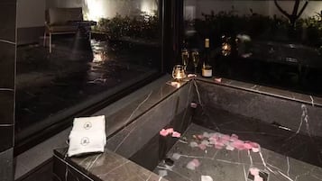 A marble-floored bathroom with a bathtub, a towel, and rose petals on the floor.
