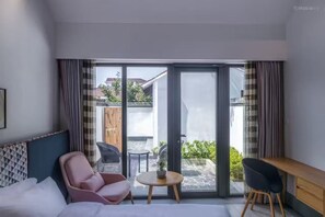 A modern hotel room with a bed, a desk, a chair, and a small table.