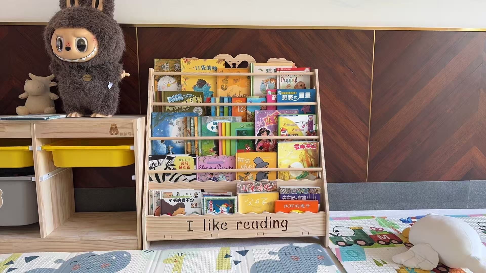 Una estantería infantil llena de libros de colores, un peluche y un estante de madera con el texto 'I like reading'.