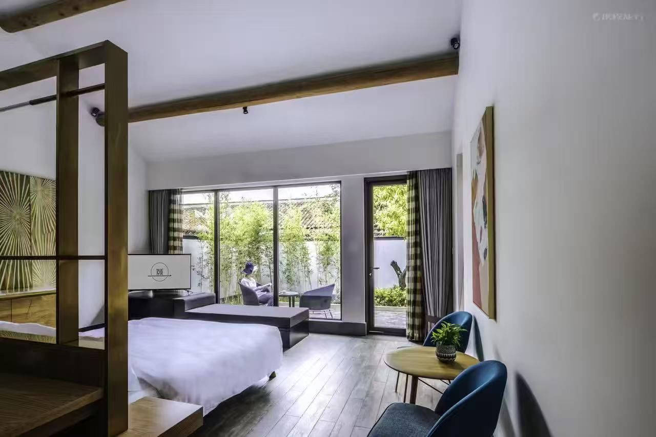 A modern hotel room with a large bed, a desk, and a view of the outdoors.