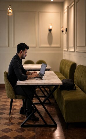 Una persona sentada a una mesa con una computadora portátil, en una habitación con piso estampado, asientos tapizados en verde y luminarias fijadas a la pared.