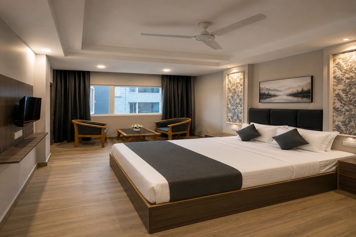 Una habitación de hotel con una cama grande, un escritorio, dos sillas, un televisor y un ventilador de techo.