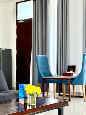 A hotel room with a dining area, a table with chairs, and a vase with yellow flowers on the table.