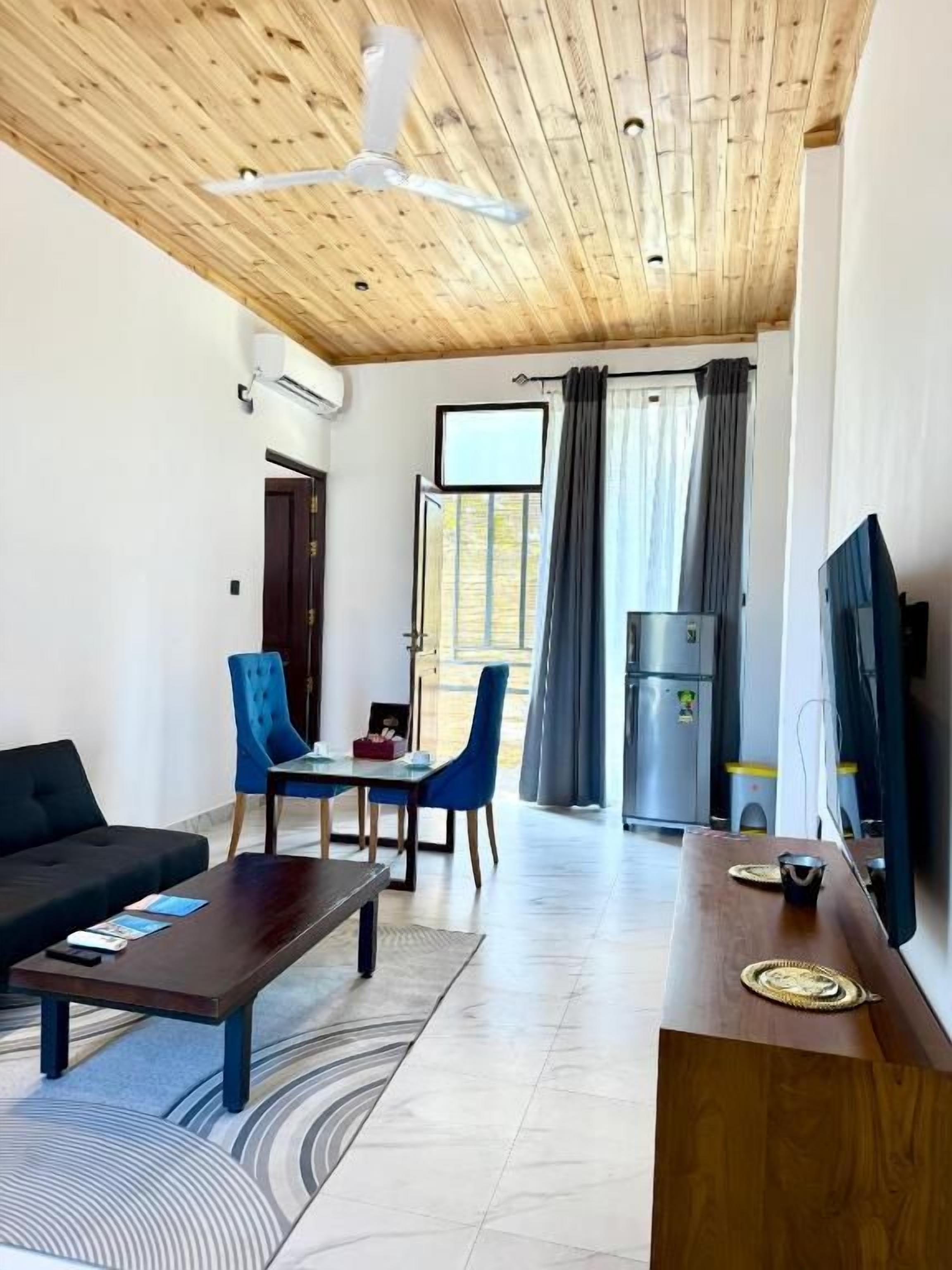 Un soggiorno moderno con soffitto in legno, una TV a schermo piatto, un divano, un tavolino da caffè e un'area pranzo con sedie e tavolo.