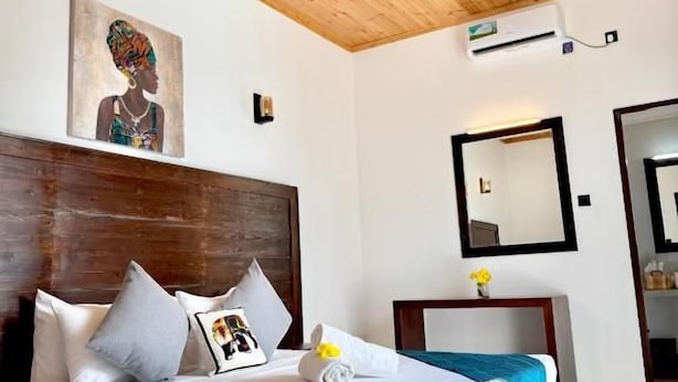 A hotel room with a wooden ceiling, a bed with white bedding, a ceiling fan, a wall-mounted mirror, and a painting. - Clear point studio  (Dikwella)