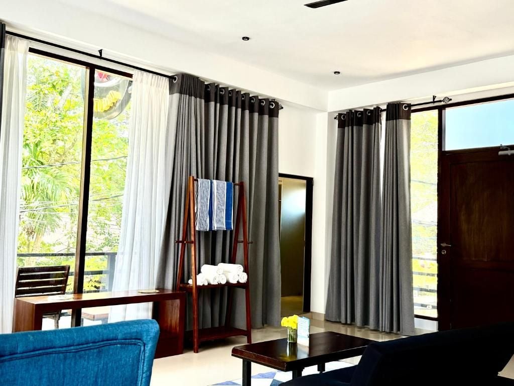 Ein Zimmer mit großem Fenster, einem Holztisch, einem blauen Stuhl und einem dunkelgrauen Sofa.