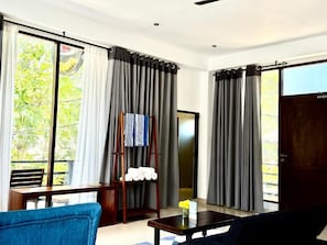 A room with a large window, a wooden table, a blue chair, and a dark-colored sofa.