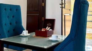 A room with a glass table, two blue chairs, a wooden door, and a window with a view. - Clear point studio  (Dikwella)