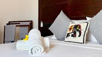 Habitación de hotel con techo de madera, una cama grande con almohadas, un cuadro sobre la cama y una pequeña almohada con motivos de elefante.