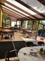 Un comedor interior con mesas y sillas de madera, ventanas amplias y piso de baldosas.