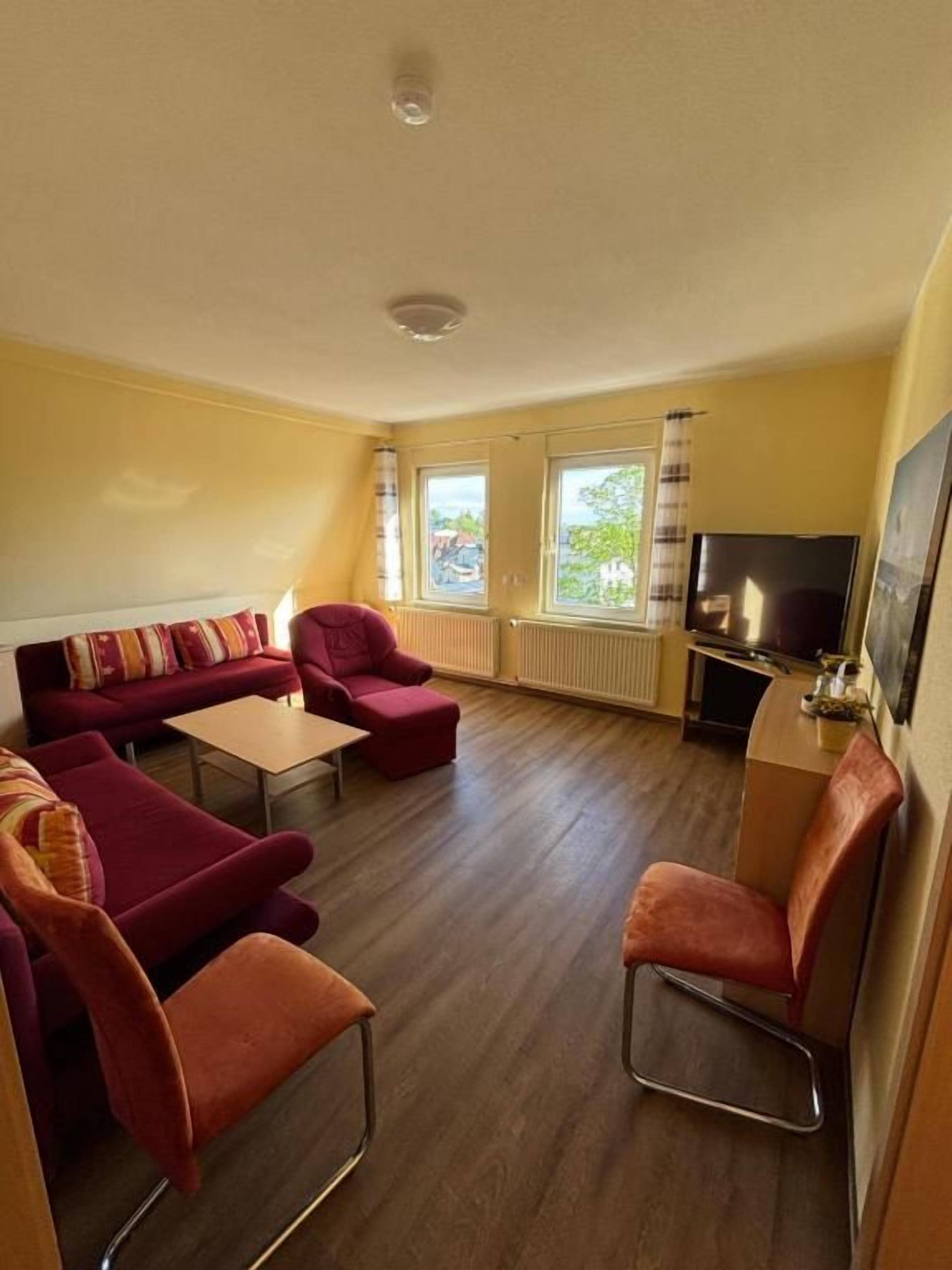 Una sala de estar con sofá, sillas, una mesa de centro, televisor y ventanas.