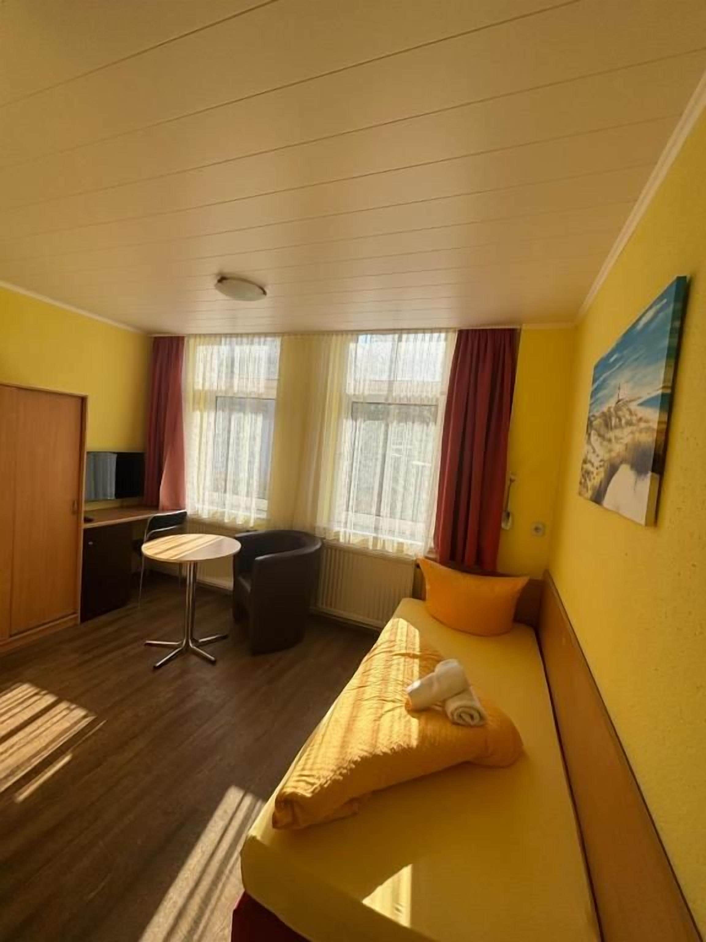 Quarto de hotel com cama, escrivaninha, cadeira e janela com cortinas.