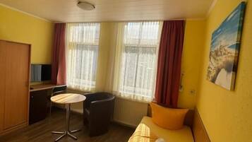 Quarto de hotel com cama, escrivaninha, cadeira e janela com cortinas.
