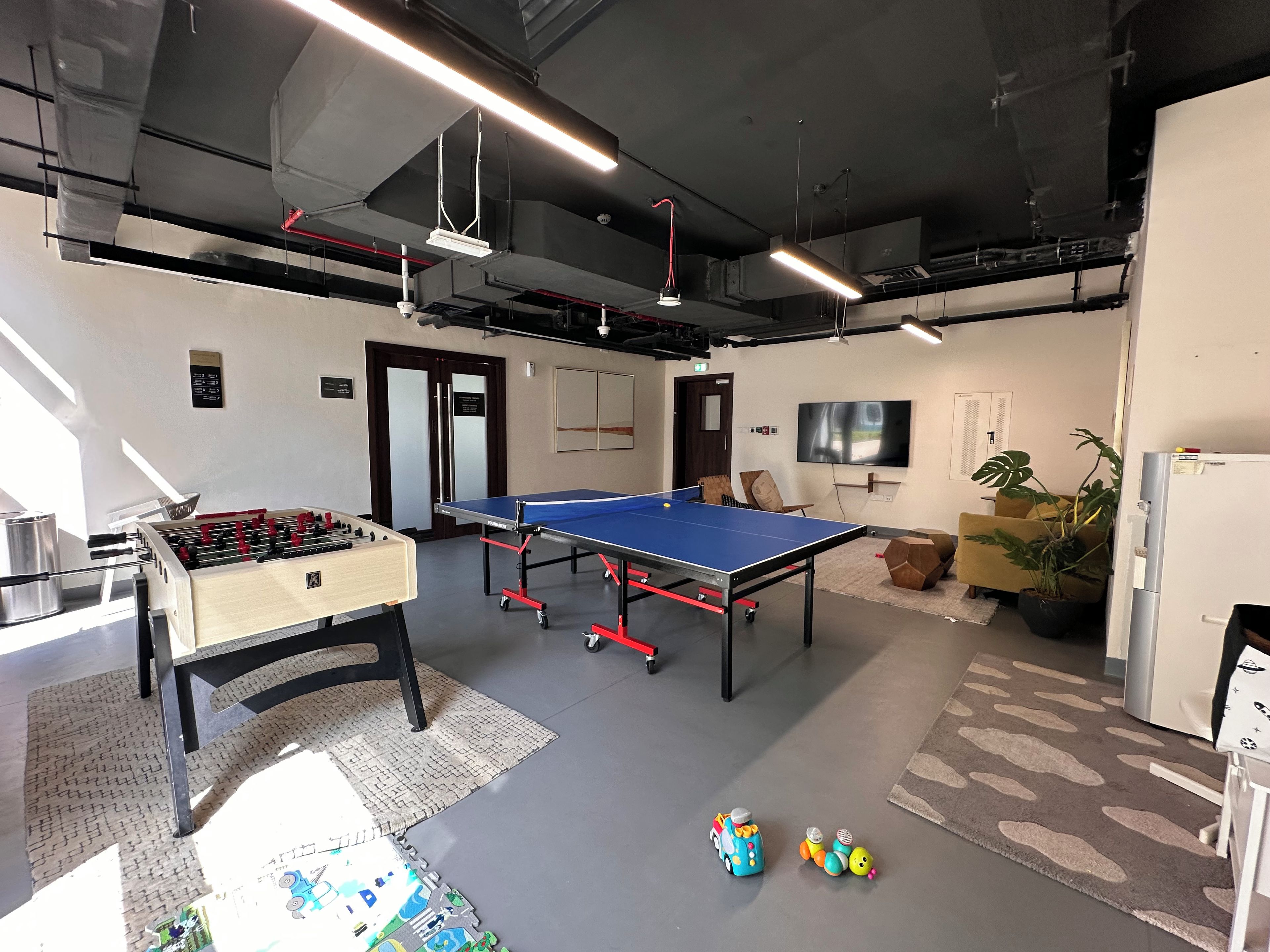 Une pièce équipée d’une table de ping-pong, d’un baby-foot et d’un téléviseur fixé au mur.
