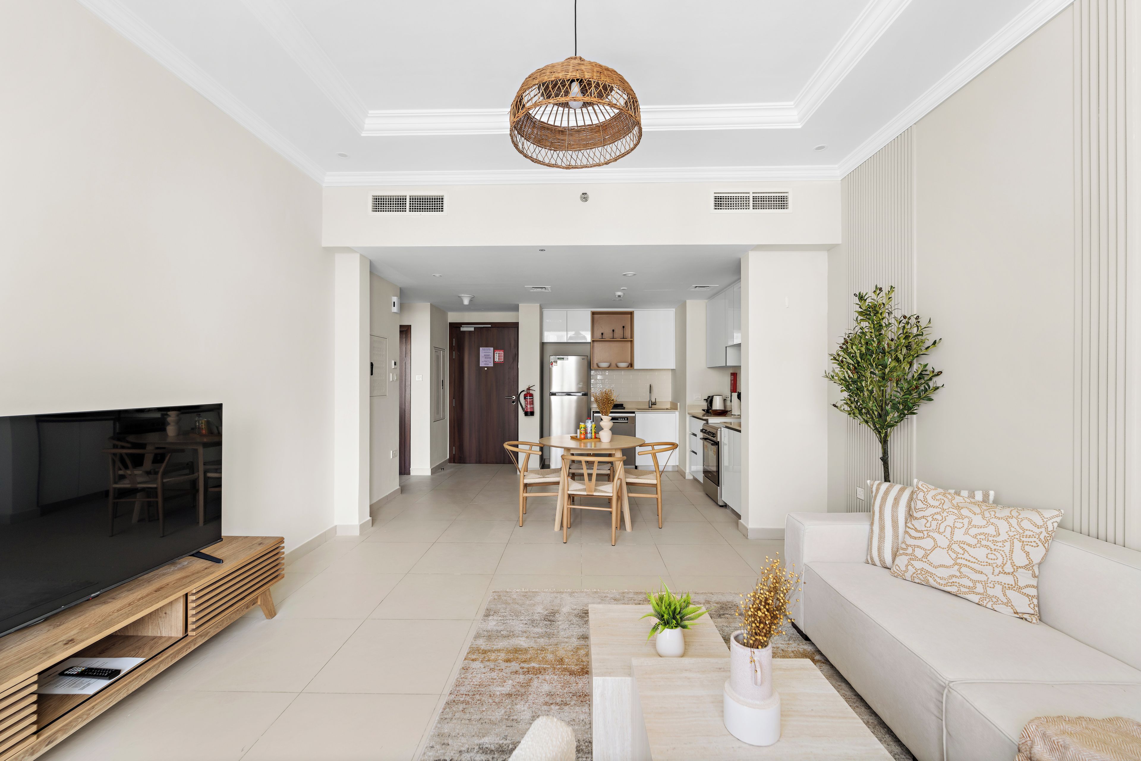 A modern living room with a flat-screen TV, wooden entertainment unit, and a dining area with a table and chairs.