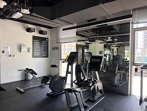 A gym with exercise equipment, a mirror, and a window with a city view. - Vogue | Reflection near Reem Central Park & Beach (Abu Dhabi)