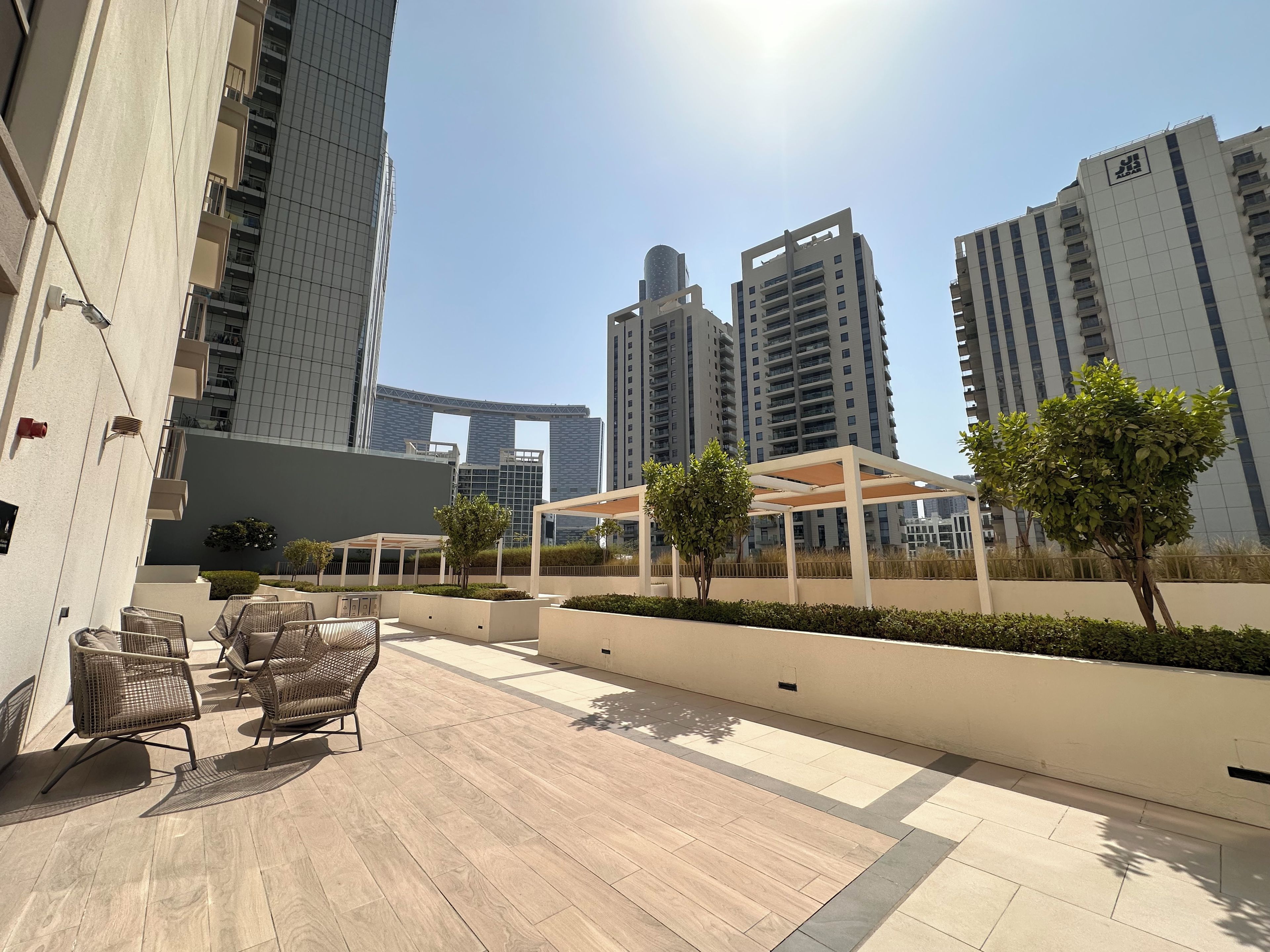 A rooftop terrace with outdoor seating, a pergola, and a view of surrounding high-rise buildings.