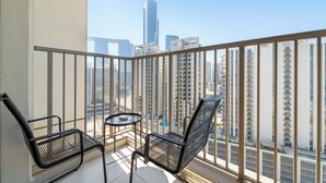 Un balcón con dos sillas y una mesita, con vistas a un paisaje urbano con edificios altos.
