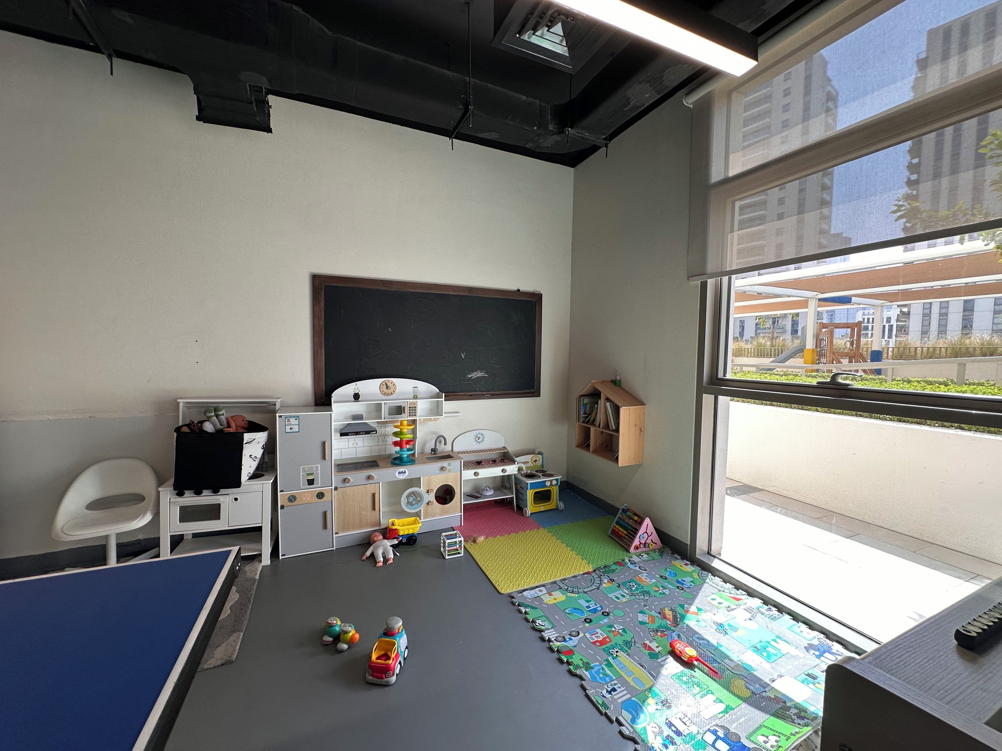 Une salle de classe avec un tableau noir, un espace de jeux et une vue sur l’extérieur par la fenêtre.