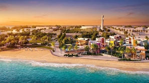 A coastal resort with beachfront villas, palm trees, and a prominent tower structure. - Vogue | Reflection near Reem Central Park & Beach (Abu Dhabi)