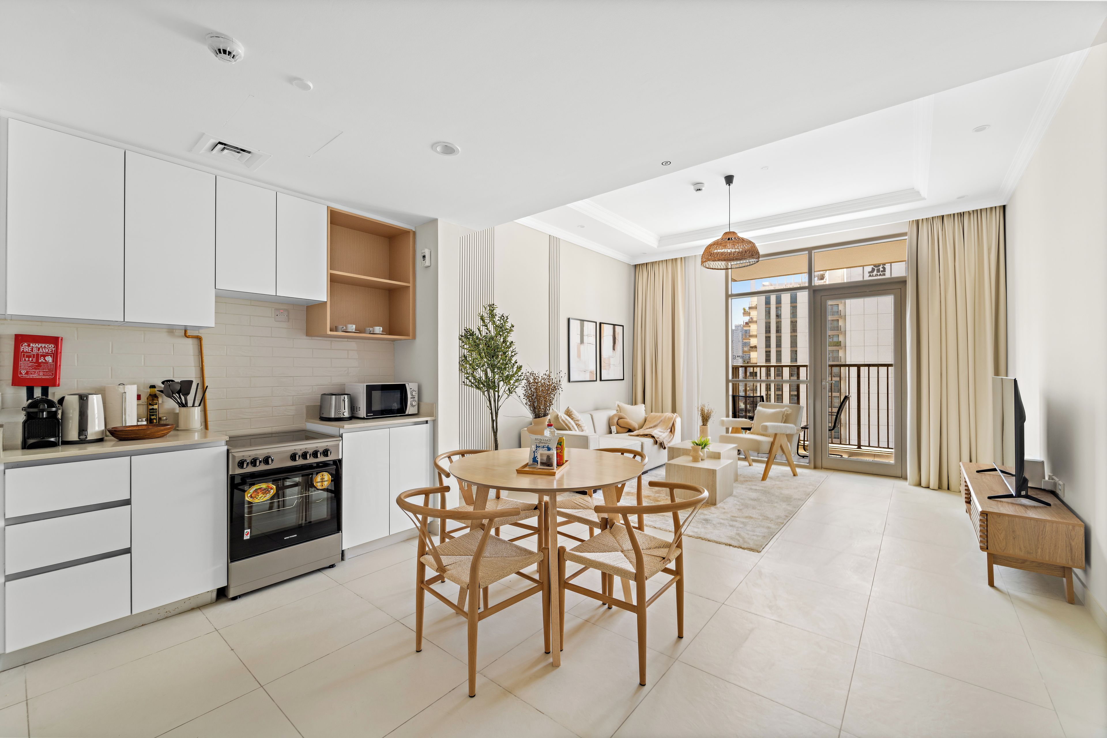 A modern kitchen with white cabinets, a built-in oven, and a dining area with a round table and chairs.