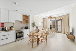 A modern kitchen with white cabinets, a built-in oven, and a dining area with a round table and chairs. - Vogue | Reflection near Reem Central Park & Beach (Abu Dhabi)