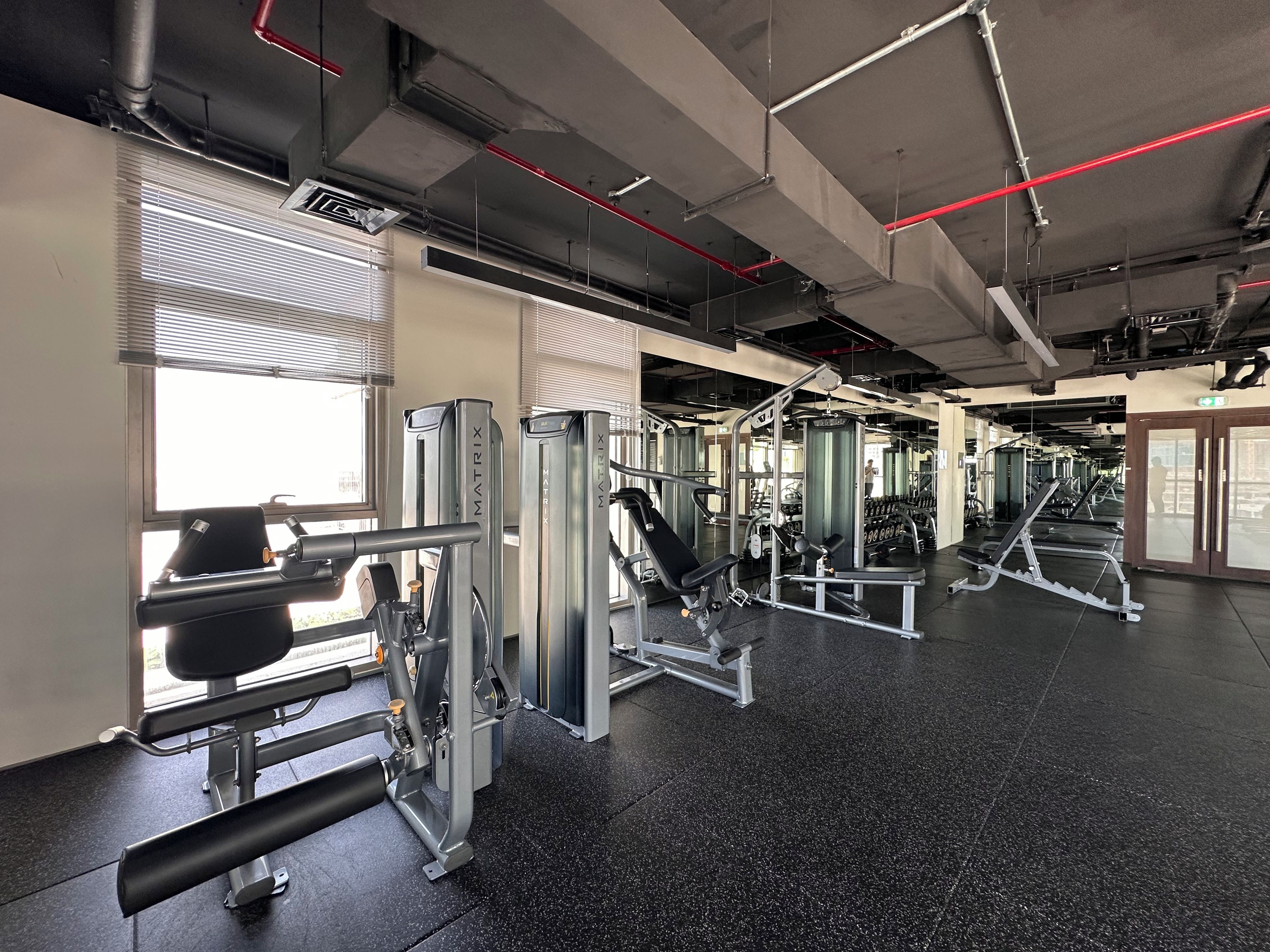 A gym with various exercise machines, large windows, and a speckled black floor.