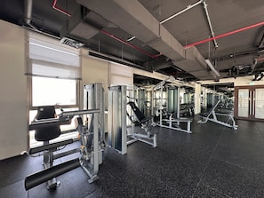 A gym with various exercise machines, large windows, and a speckled black floor. - Vogue | Reflection near Reem Central Park & Beach (Abu Dhabi)