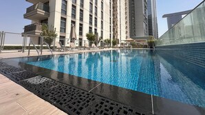 Una piscina con sillas de descanso y un rascacielos al fondo.