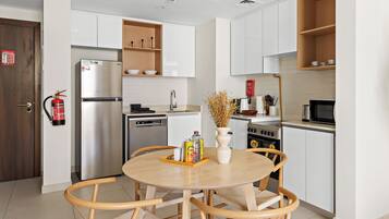 Une cuisine moderne avec des meubles blancs, un réfrigérateur en acier inoxydable et un coin repas comprenant une table ronde et des chaises en osier.