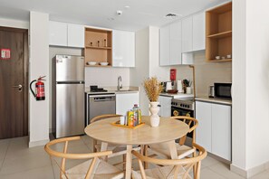 A modern kitchen with white cabinets, a stainless steel refrigerator, and a dining area with a round table and wicker chairs. - Vogue | Reflection near Reem Central Park & Beach (Abu Dhabi)