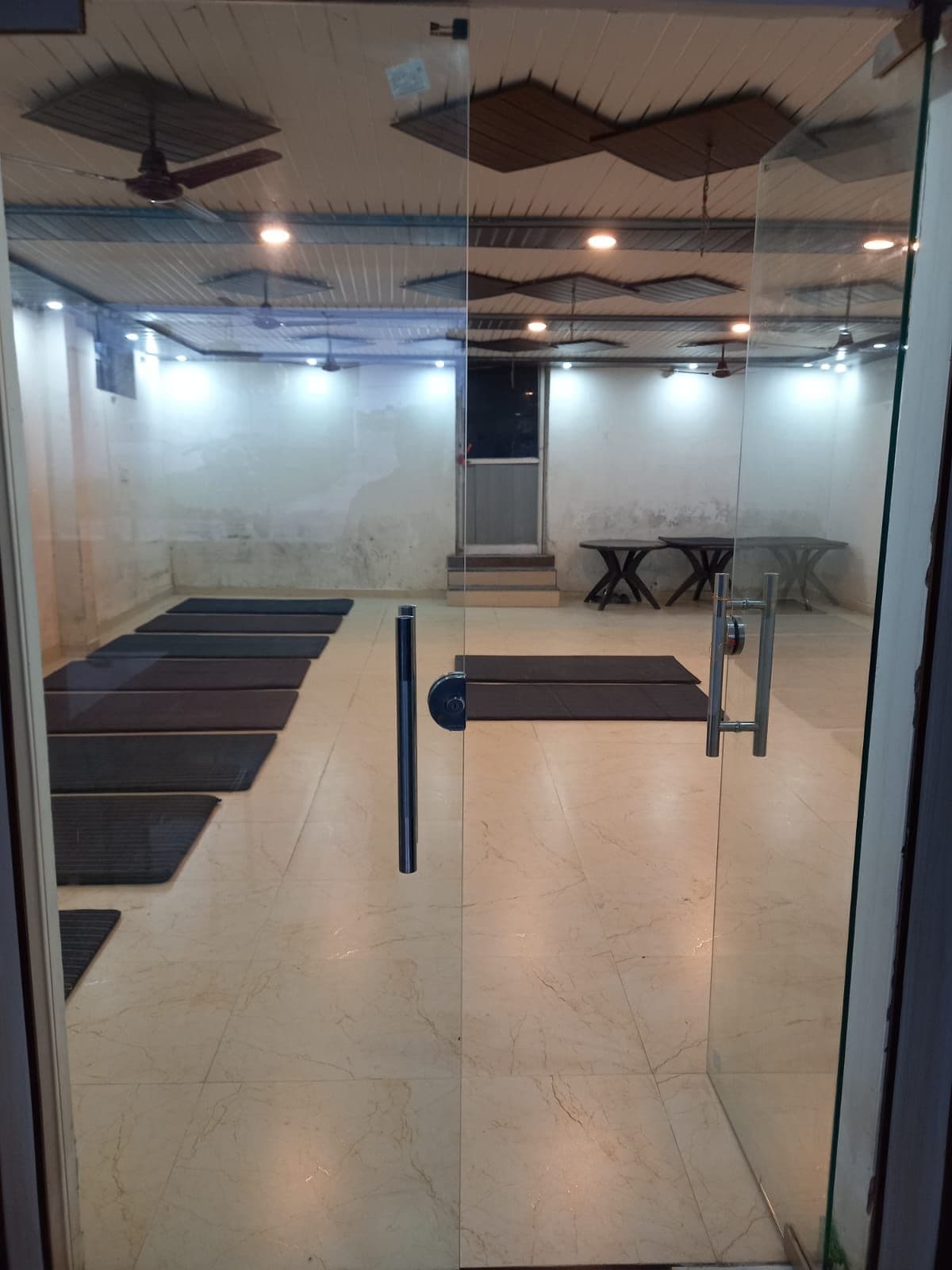 Una habitación con puerta de vidrio, ventilador de techo, una mesa con sillas y un tapete en el suelo.