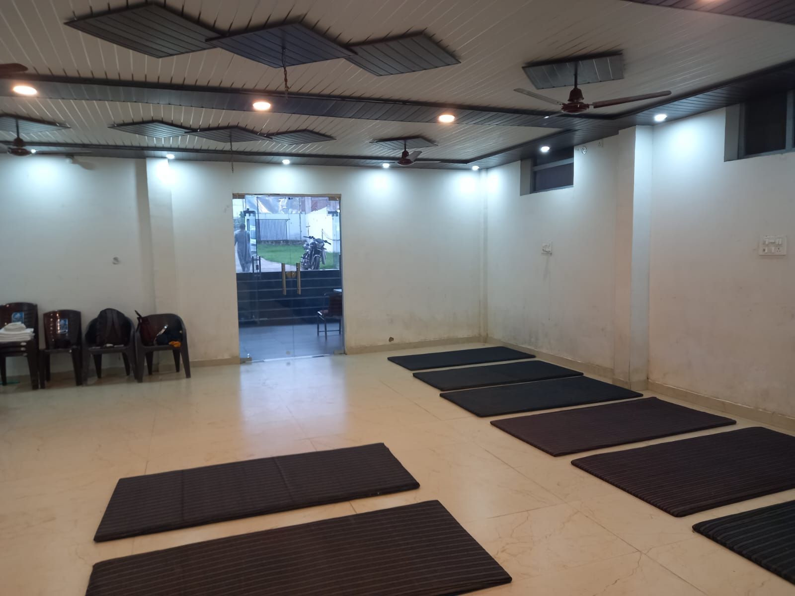 A room with ceiling fans, a large window, and exercise mats arranged in rows.
