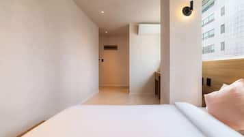 A modern hotel room with a bed, a nightstand, a wall-mounted light, and a view of a building outside.