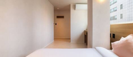 Habitación de hotel moderna con cama, mesita de noche, lámpara de pared y vista a un edificio.