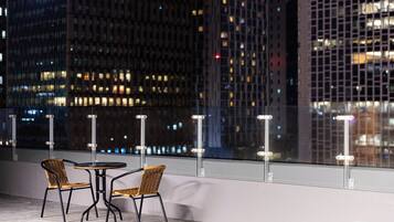 Terraza en la azotea con dos sillones de mimbre y una mesa pequeña, con vistas a un paisaje urbano nocturno.