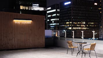 A rooftop terrace with a wooden wall and a sign that reads 'stay myomi.' There are two wicker chairs and a small table.