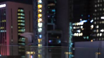 A nighttime cityscape with illuminated buildings and a bar area with chairs.
