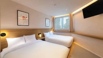 A hotel room with two beds, a large window with a view, a flat-screen TV mounted on the wall, and a framed artwork on the wall.