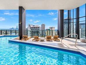 A rooftop infinity pool with lounge chairs, a city skyline view, and modern architecture. - Stunning Broadbeach 1BR with Sweeping City Views (Gold Coast)