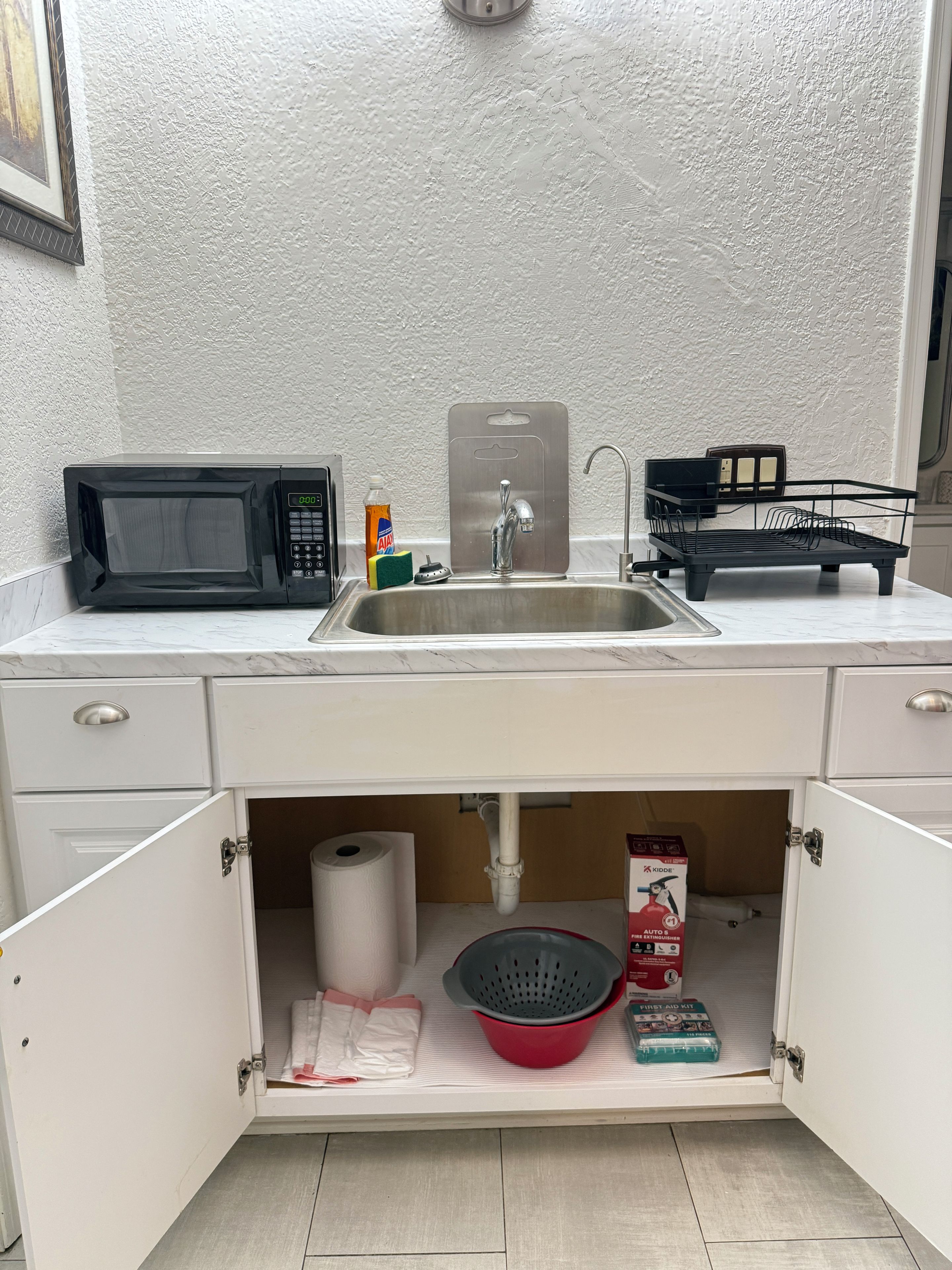 Una cocina con microondas, lavamanos y armarios de almacenamiento.