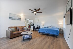 Un dormitorio moderno con una cama, un sofá, una mesa de comedor y un ventilador de techo.