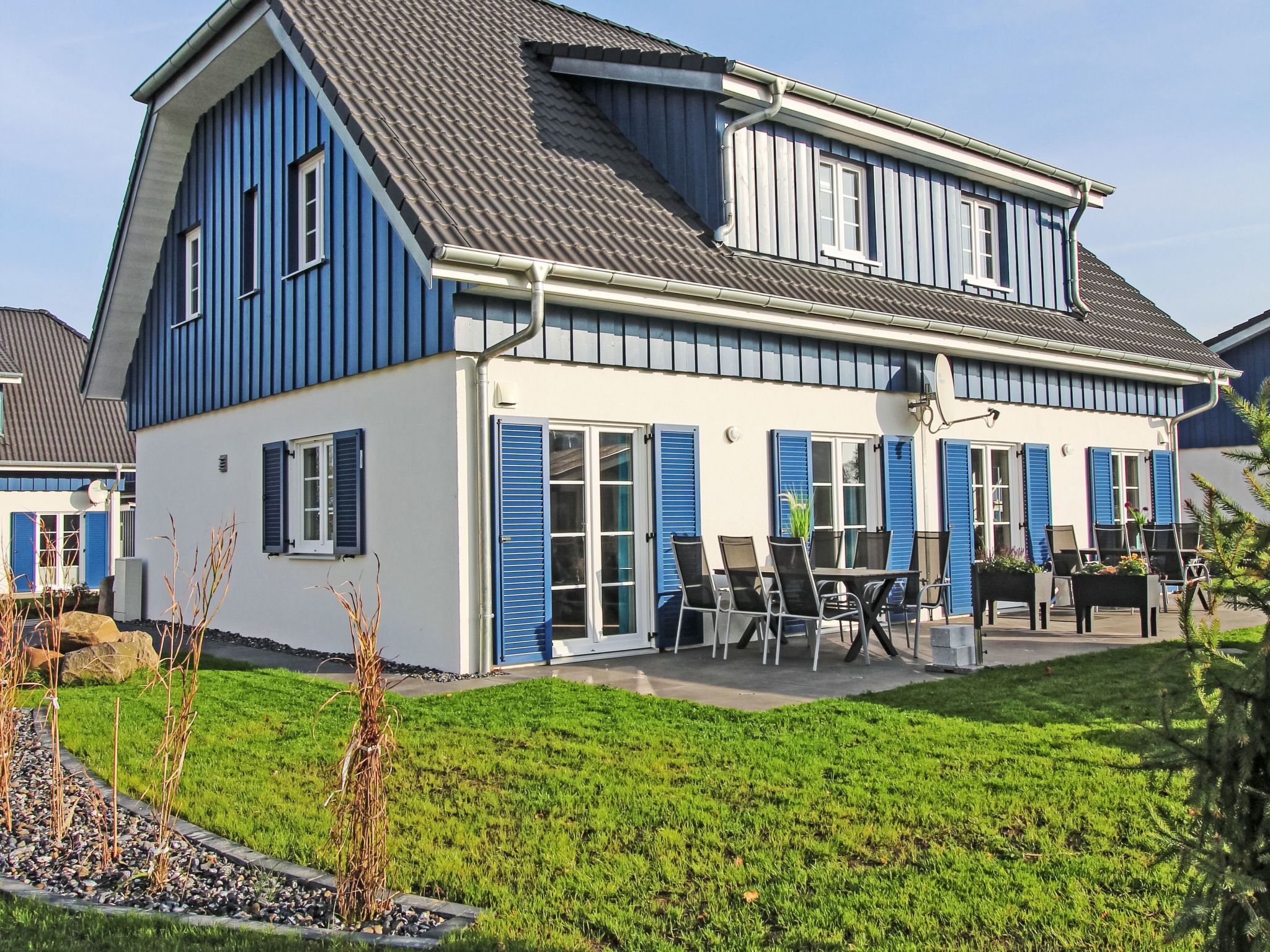 Een huis met twee verdiepingen, een balkon, een terras met tuinmeubilair en een verzorgd gazon.